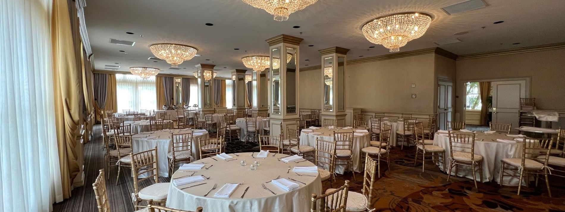 Round tables by gold chairs under crystal chandeliers in Crystal Ballroom at Warwick Melrose Dallas