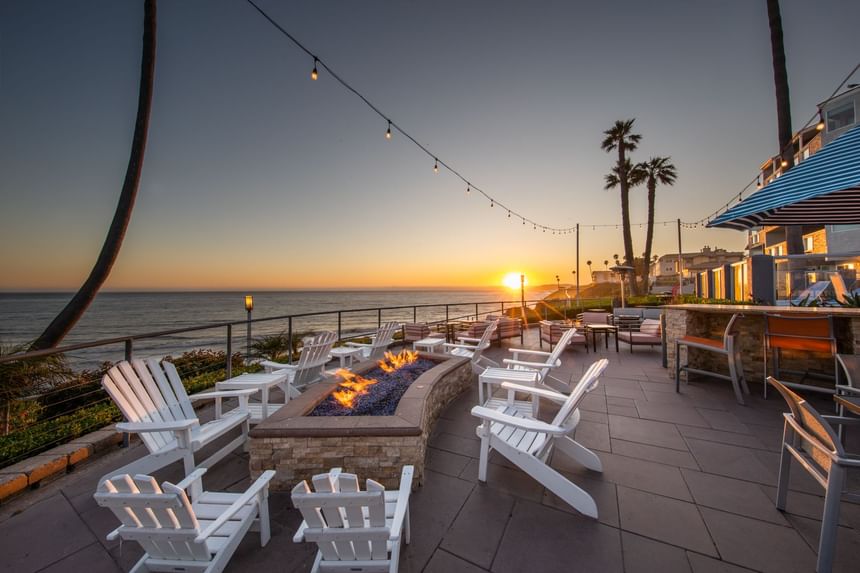 Fire pit at sunset on the ocean with white Adirondack chairs