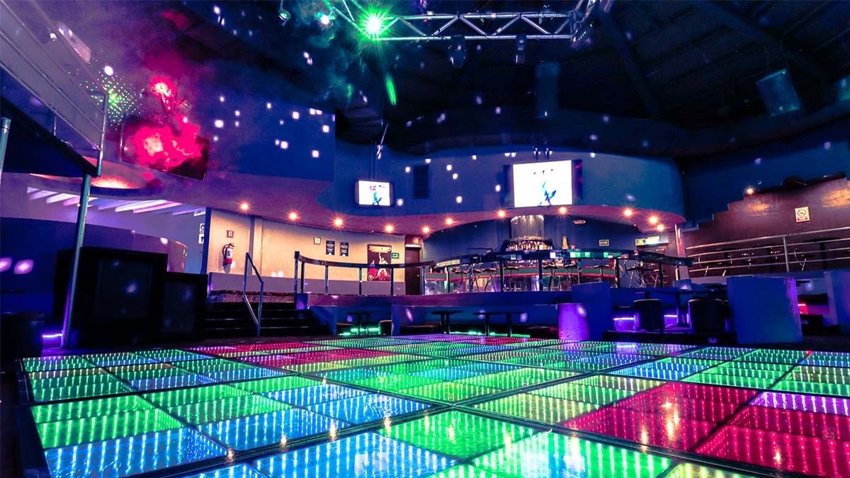 Pista de baile vacía con baldosas LED brillantes bajo focos de techo en El Rollo de Araiza Palmira 