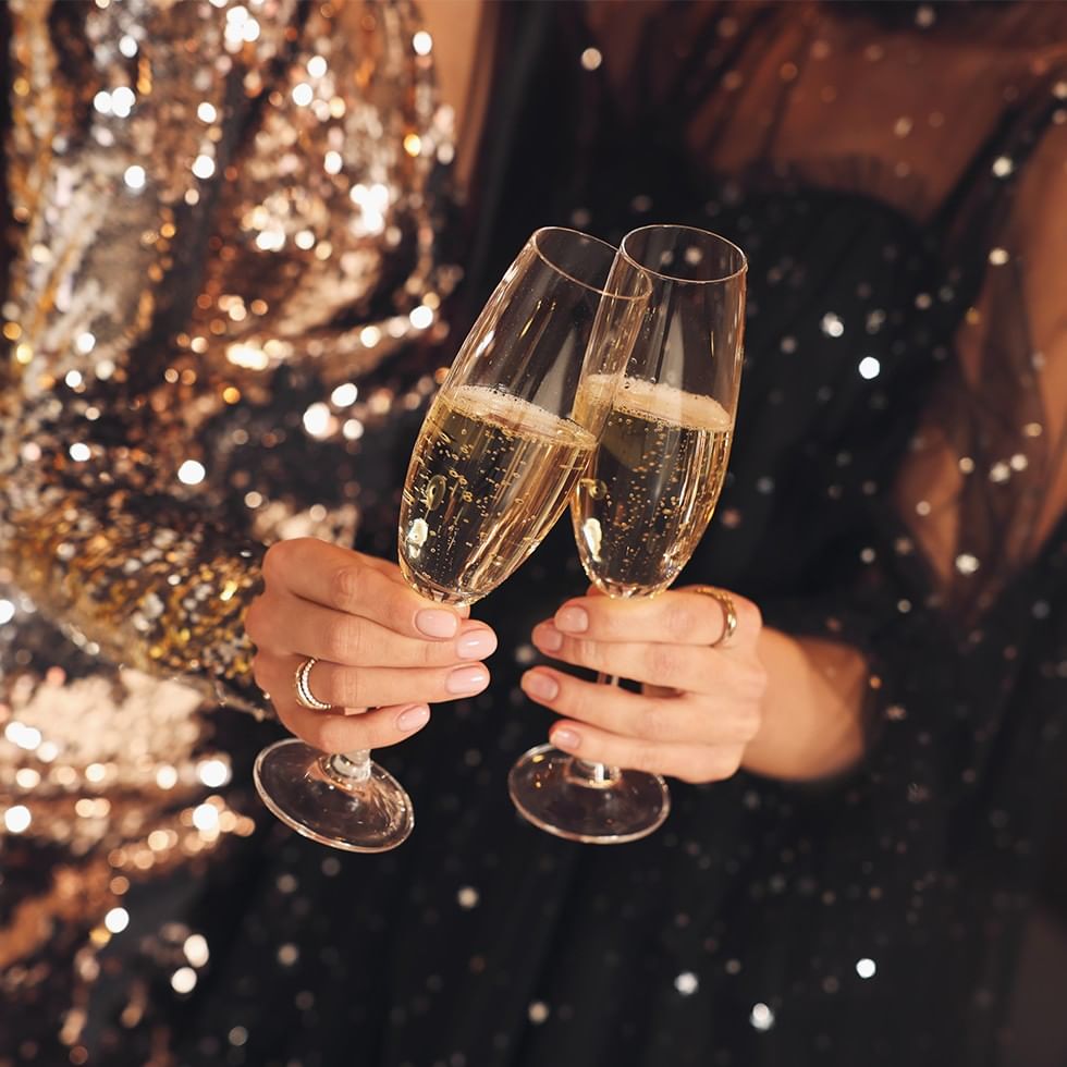 Zwei Sektgläser voller Champagner, gehalten von zwei Frauen, zum Bergsilvester.