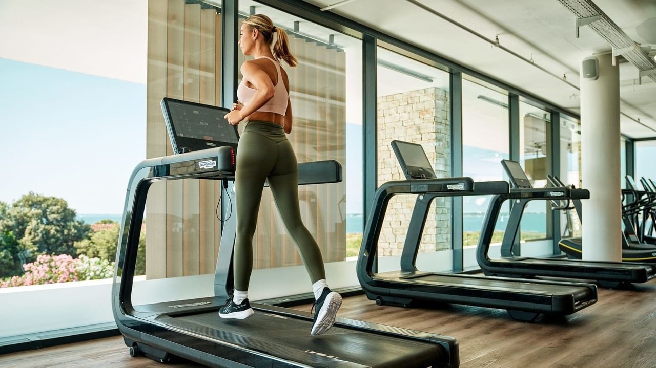 Donna in palestra su tapis roulant con finestre e vista sull'oceano.