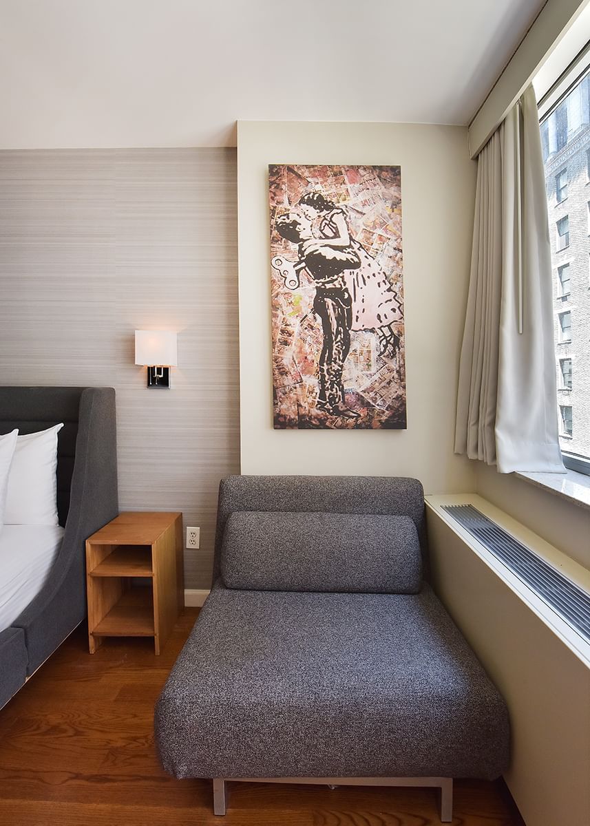 A hotel room with a gray sofa, wooden nightstand, and a painting of a couple on the wall.