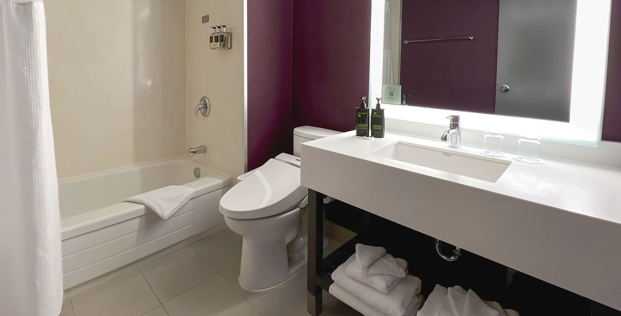 Hotel washroom with toilet, bathtub, sink, towels, and soap