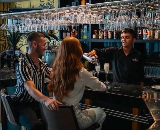 Bartender servindo drinks para casal no bar moderno com taças suspensas e arte de parede no Cumbres Lastarria