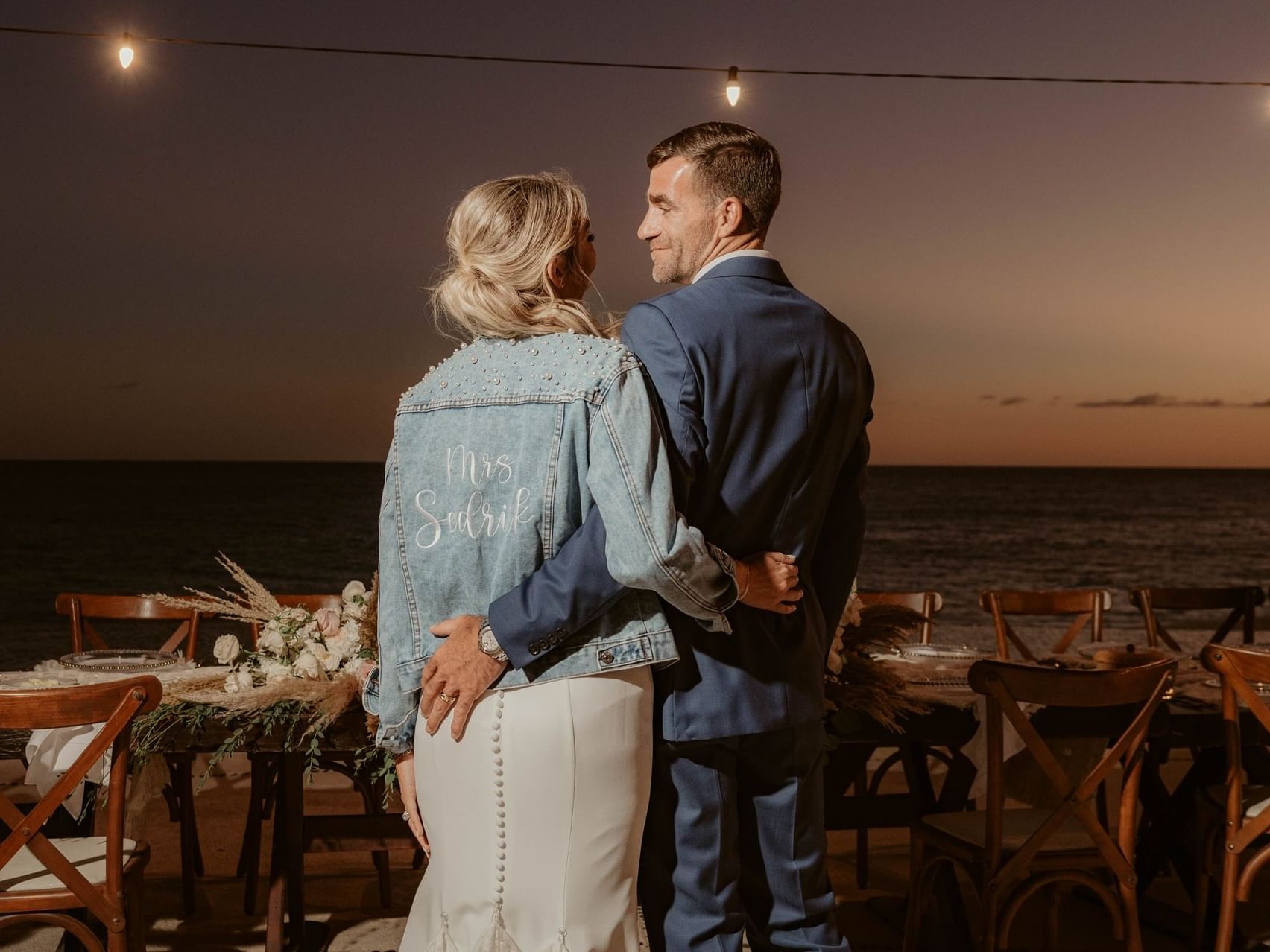 Loving couple embracing with ocean in the background at Marquis Los Cabos Resort, bride wears a personalized denim jacket