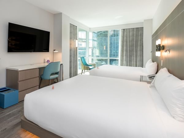 Two queen beds with white bedding, a desk, chair, and large window.