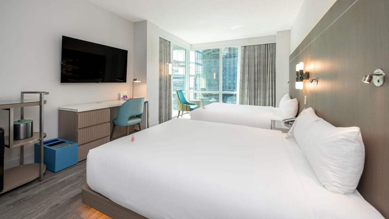 Two queen beds with white bedding, a desk, chair, and large window.