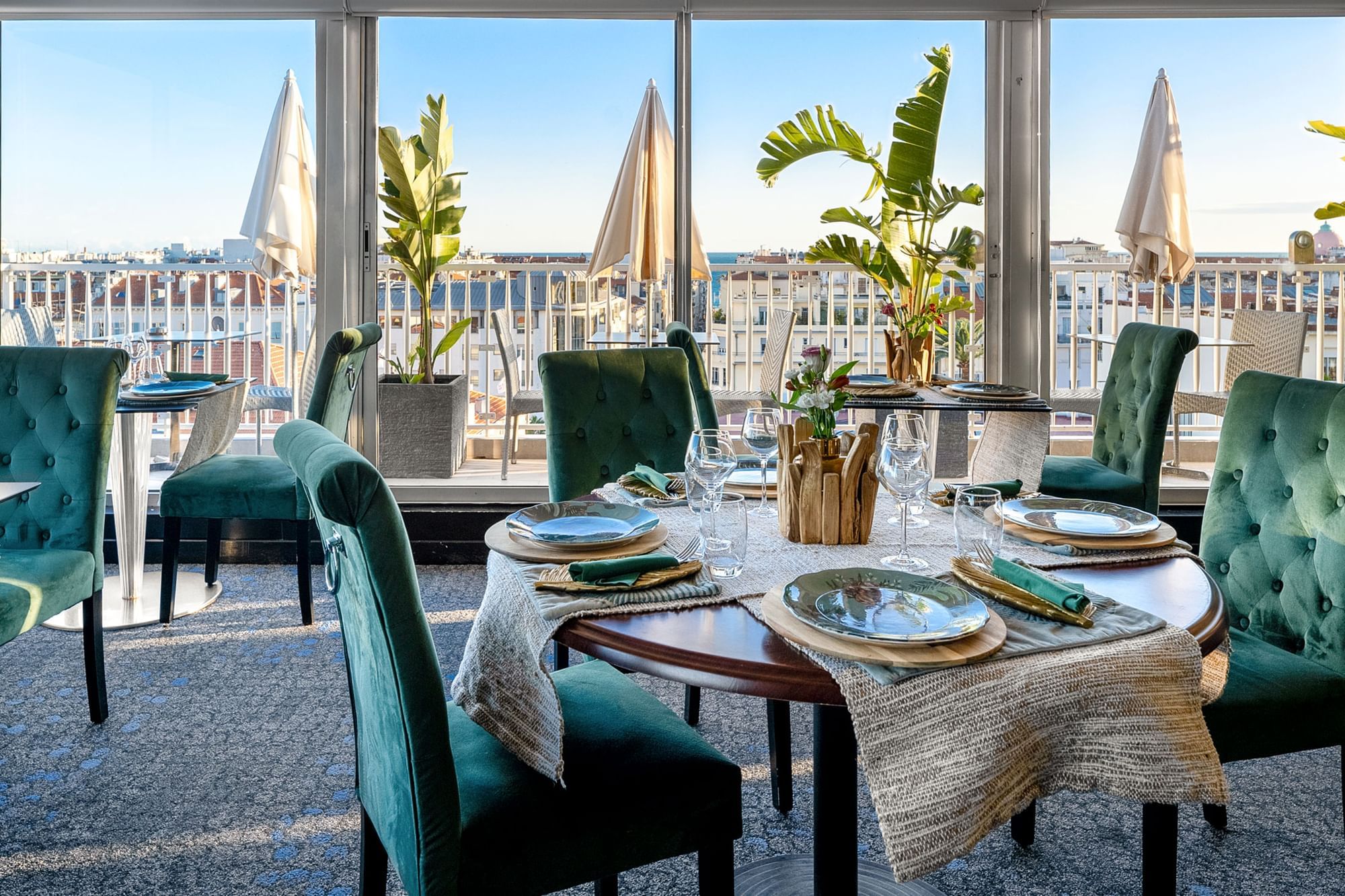 The Jungle Restaurant dining area with green velvet chairs overlooking the city from windows at Splendid Hotel & Spa Nice