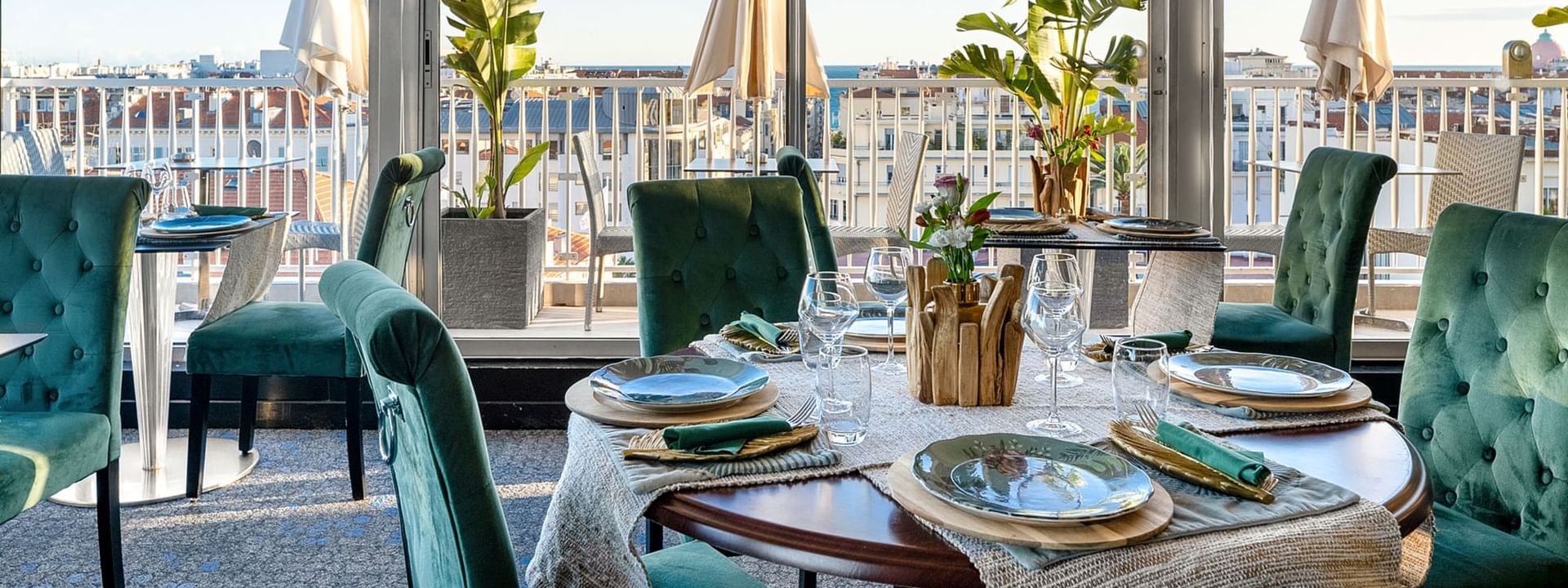 The Jungle Restaurant dining area with green velvet chairs overlooking the city from windows at Splendid Hotel & Spa Nice