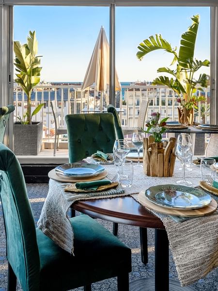 The Jungle Restaurant dining area with green velvet chairs overlooking the city from windows at Splendid Hotel & Spa Nice