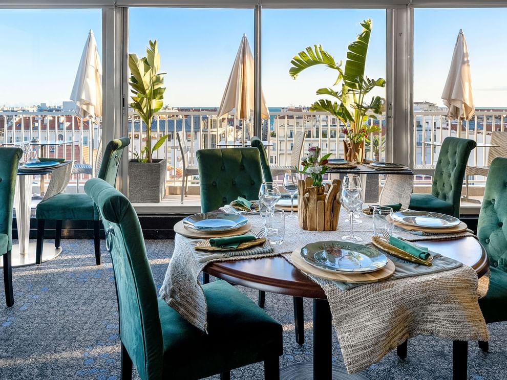 The Jungle Restaurant dining area with green velvet chairs overlooking the city from windows at Splendid Hotel & Spa Nice