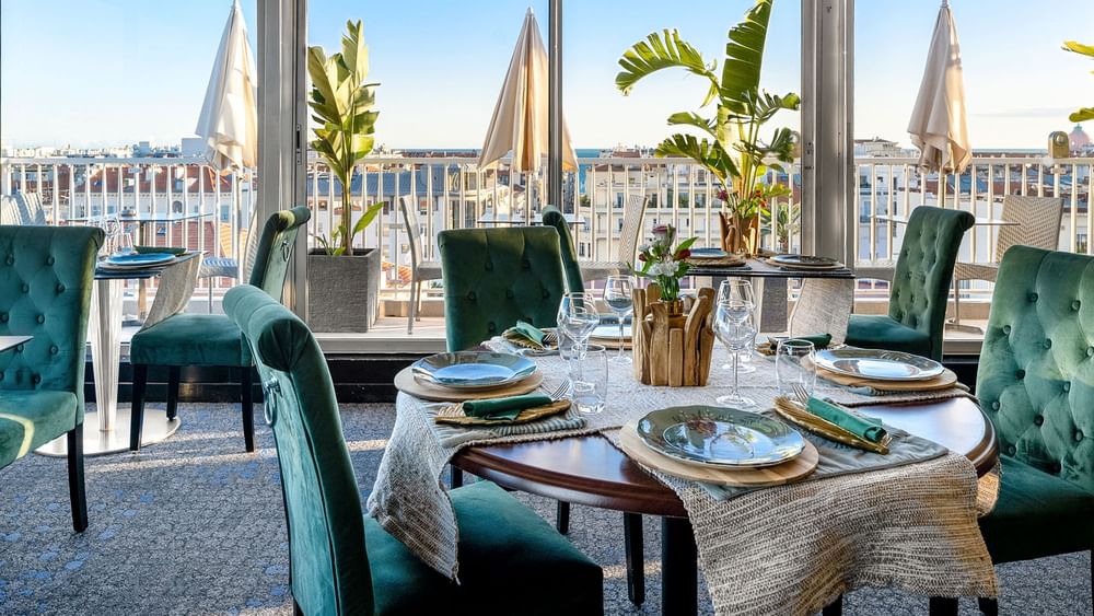 The Jungle Restaurant dining area with green velvet chairs overlooking the city from windows at Splendid Hotel & Spa Nice