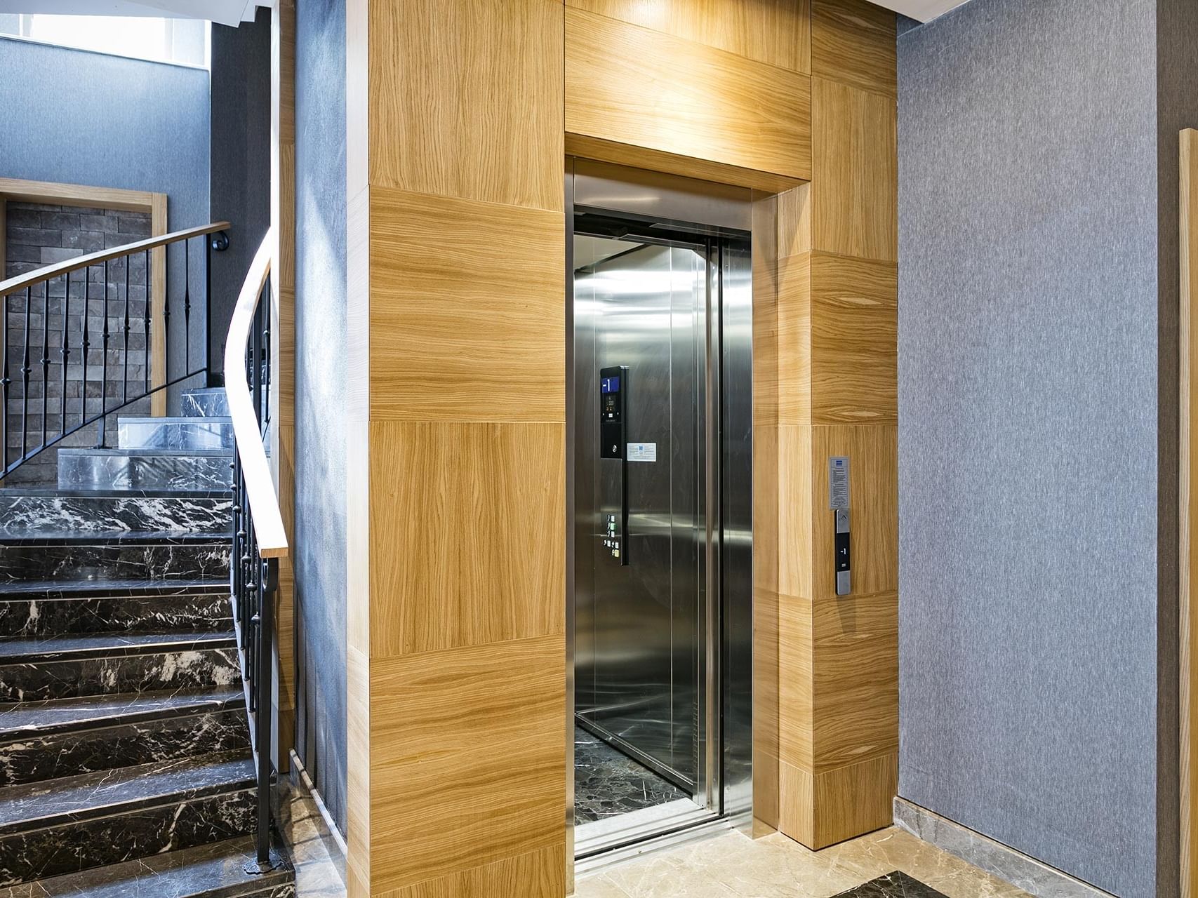 Modern interior view at Titanic Luxury Collection Bodrum featuring marble stairs and a wooden elevator door.