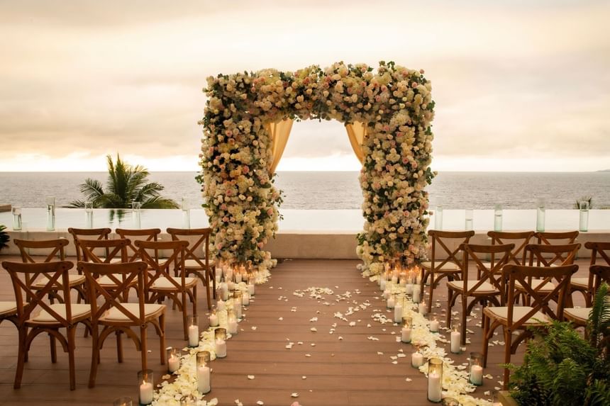 Oceanfront wedding ceremony setup with floral arch, wooden chairs, and candles at sunset at Almar LGBT Luxury Resort