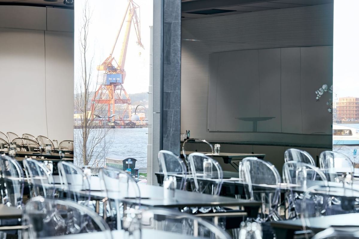 Konferensrum med bord och stolar, vattenglas och hamn med kran i fönstret.