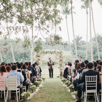 Outdoor wedding ceremony at The Saujana Hotel Kuala Lumpur with guests seated by a floral arch amid lush greenery