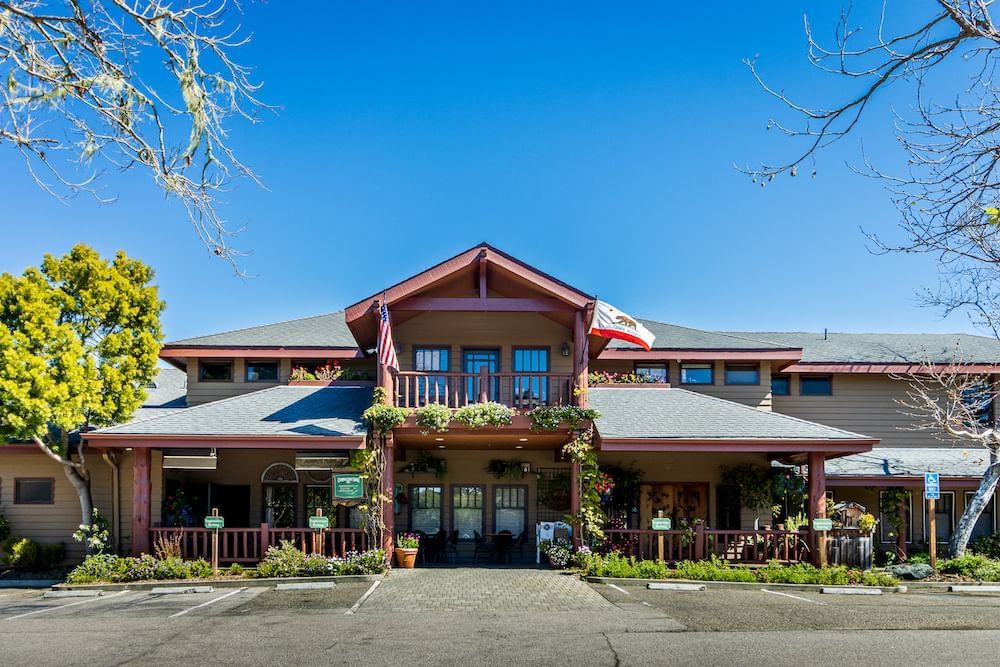 The front of a building with flags, flowers, and a patio under a clear blue sky.