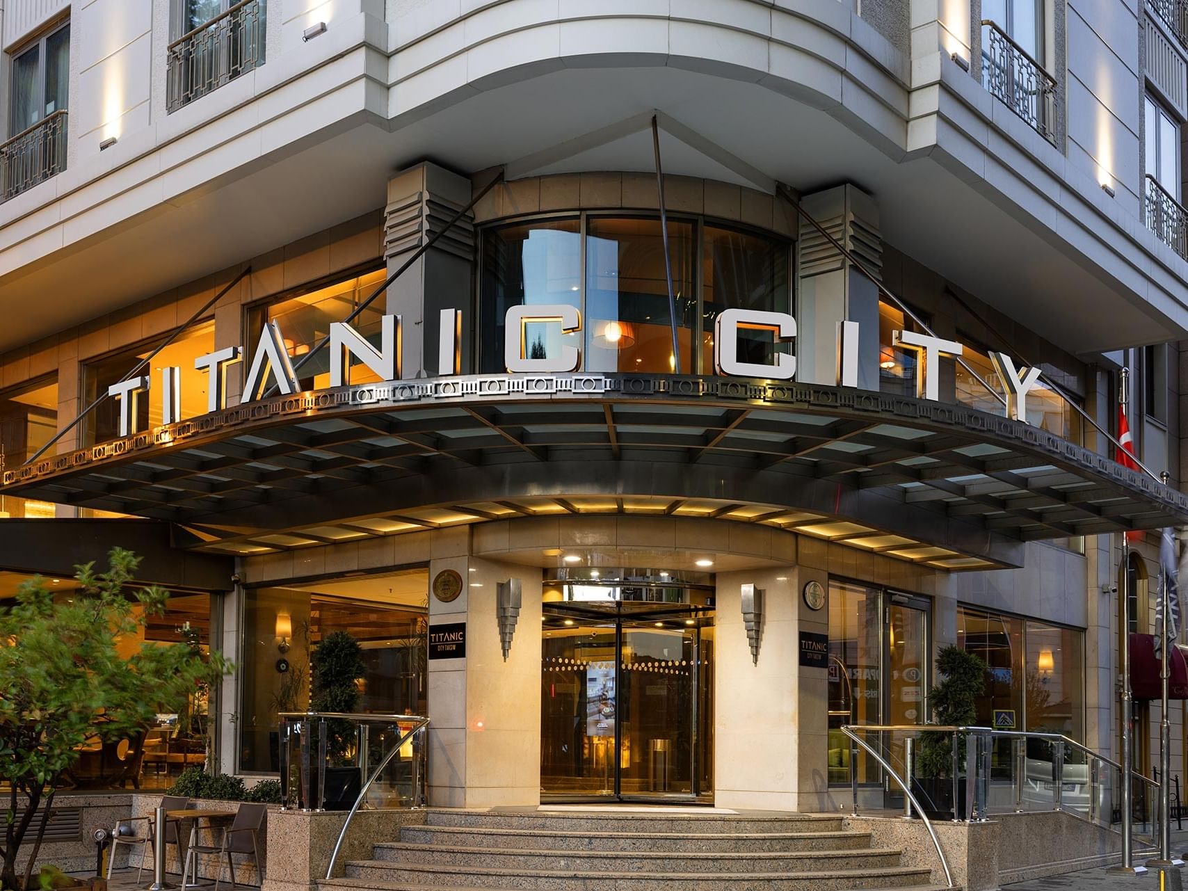 Titanic City Hotel entrance with illuminated sign, steps, glass doors, and exterior lighting.