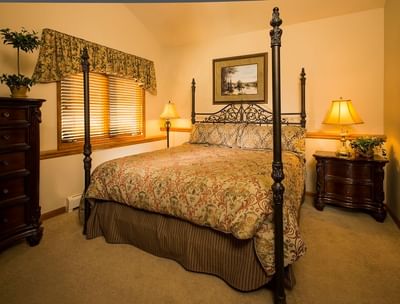 A traditional bedroom with a queen-sized, dark wood, four-poster bed and a floral comforter at The Stanley Hotel
