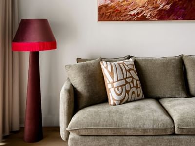 Gray couch with decorative pillow, red lamp, and abstract art in the background.