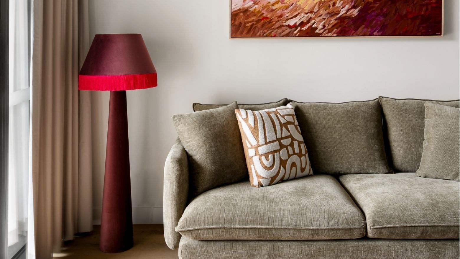 Gray couch with decorative pillow, red lamp, and abstract art in the background.