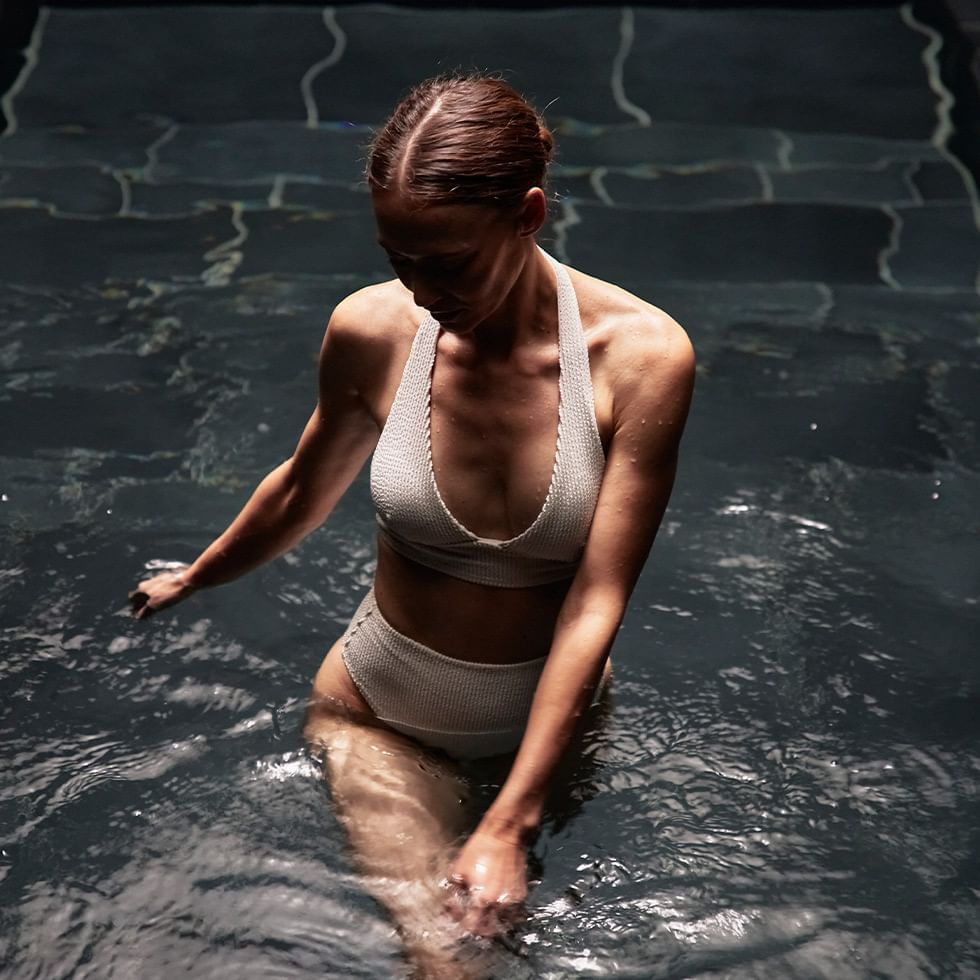 A woman in a white bikini is standing in water in a pool.