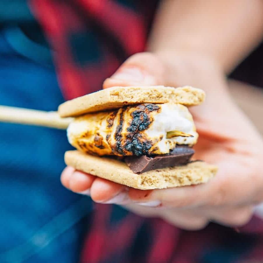 a hand holding a smores with a toasted marshmallow and chocolate