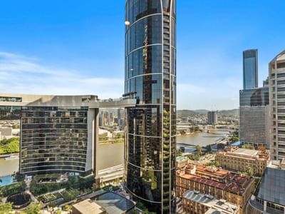 Tall modern skyscraper with surrounding buildings and a river view in an urban setting at UniLodge Brisbane City.