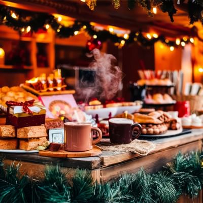 Tavolo natalizio decorato con luminarie, dolci, tè caldo e regali.