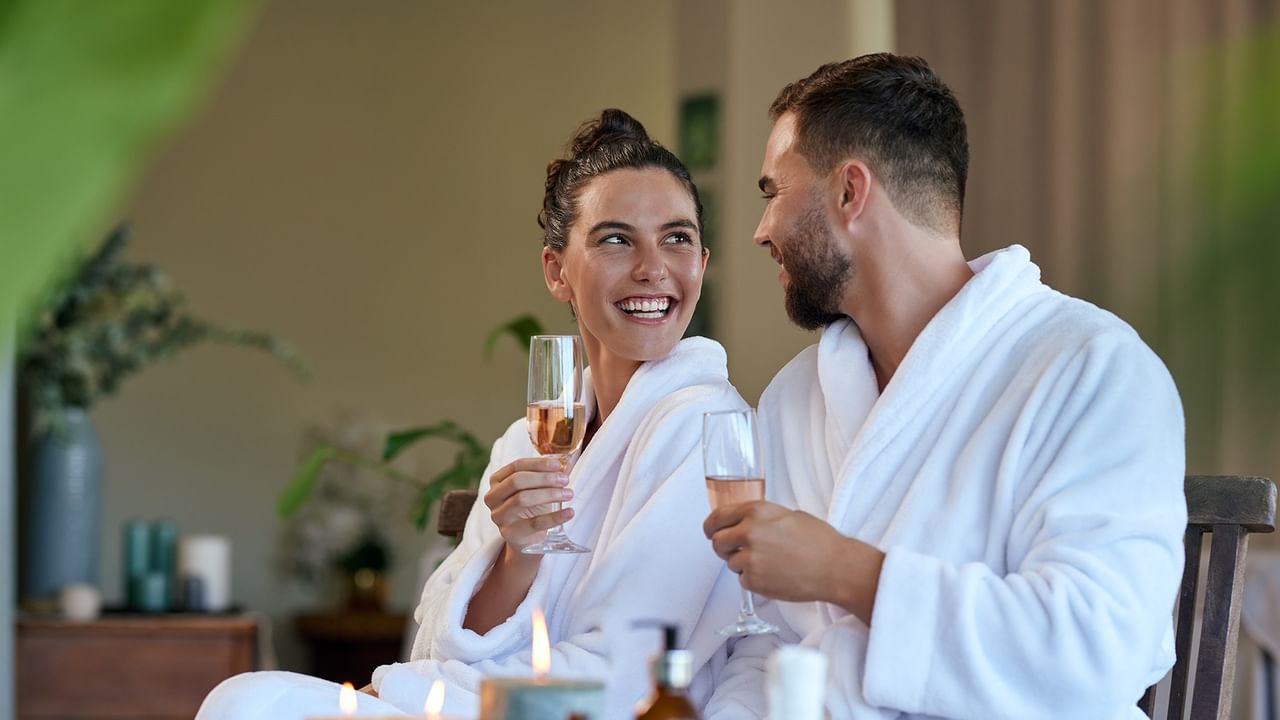 Couple in white bathrobes enjoying champagne together during a relaxing spa getaway