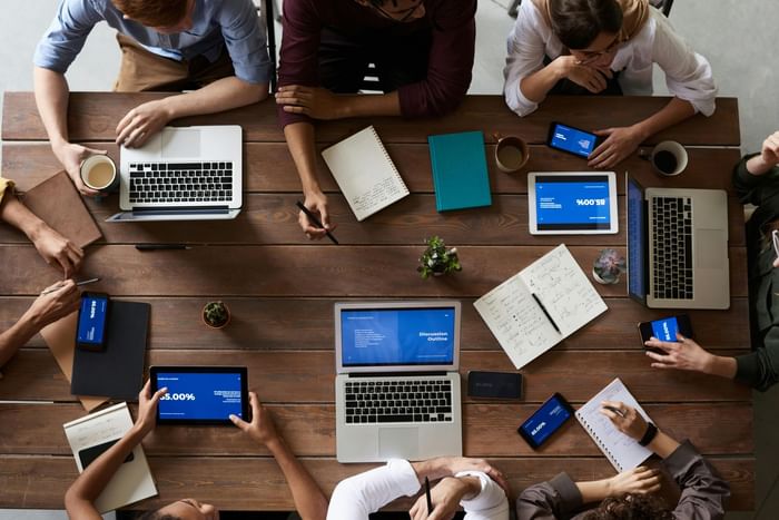 Top view of a group meeting by a wooden table, using laptops and tablets at Anaheim Portofino Inn & Suites