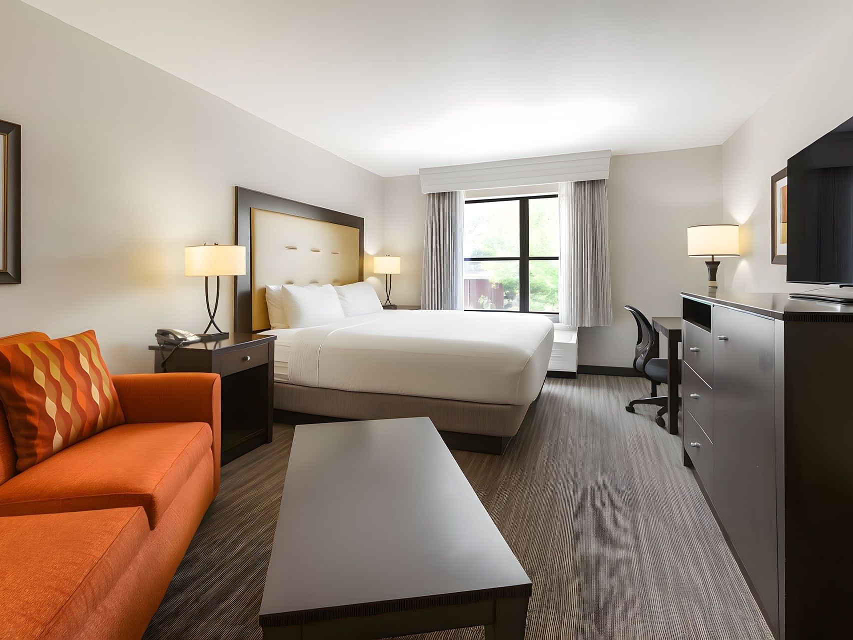 King Room with Sofa Bed featuring a king bed, orange sofa, work desk, and large window view at Branson Hillside Hotel