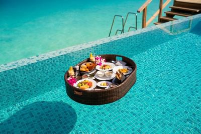 Floating basket with a lavish breakfast spread of fruits, pastries, and drinks in a clear pool at Ananea Madivaru Maldives