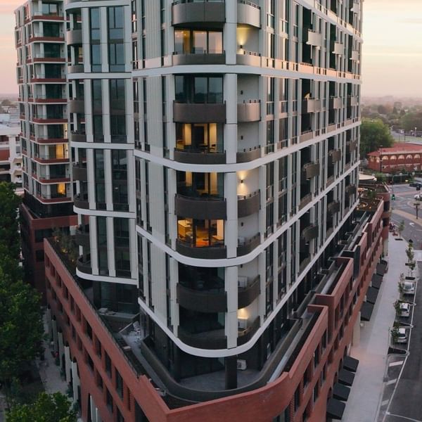 Modern urban building with balconies and cars on the road at sunset.