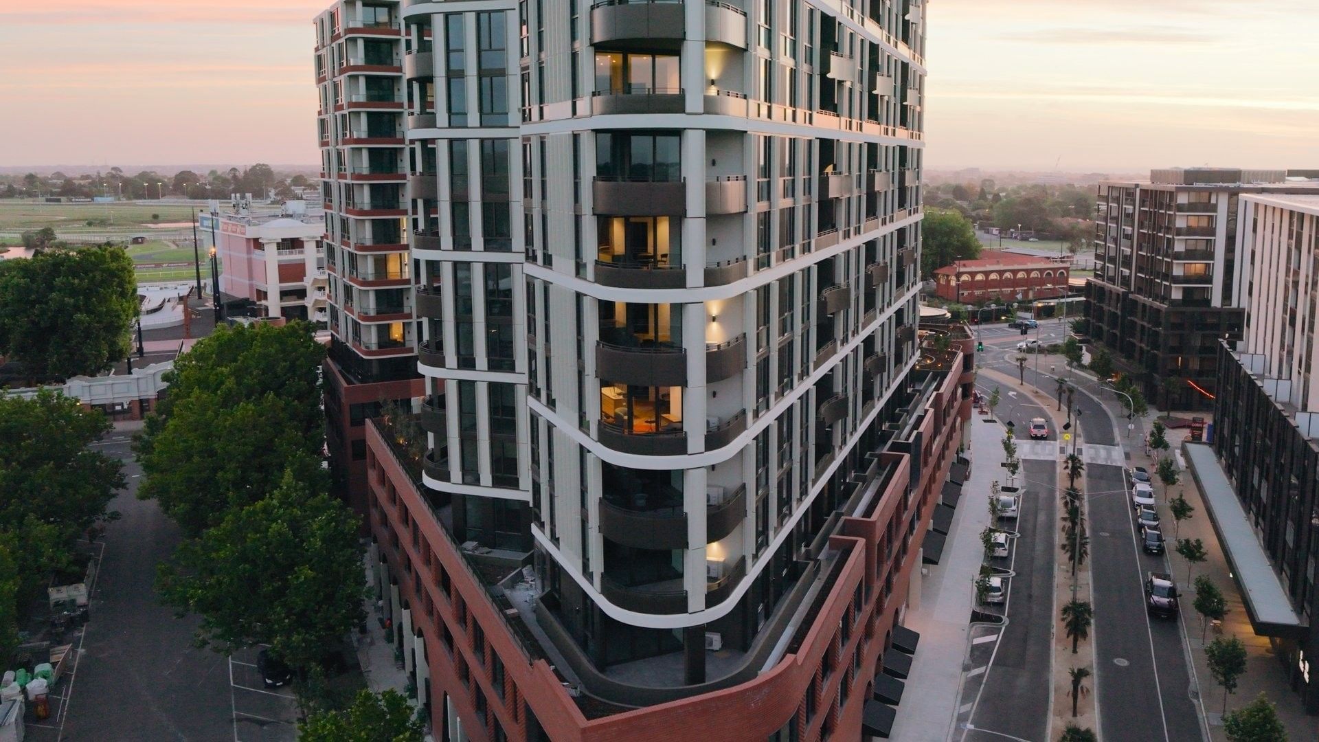 Modern urban building with balconies and cars on the road at sunset.