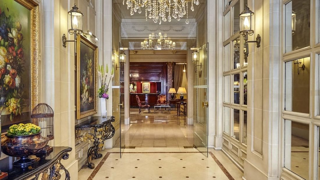 Grand hallway under a crystal chandelier with marble floors leading to a reception area at Hotel Westminster Paris