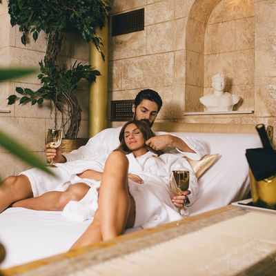 Couple laying on a bed & having champagne at Originals Hotels