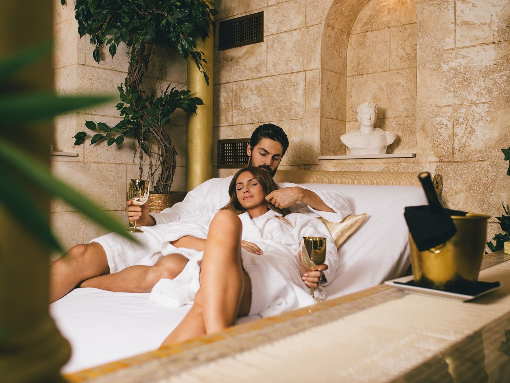 Couple laying on a bed & having champagne at Originals Hotels