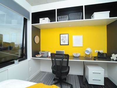Stylish room with desk, chair, and yellow accent wall at UniLodge Auckland City.