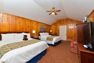 Seating area and TV facing the beds in Two Queen Beds Cabin with wooden paneling walls at Buffalo Bill Village