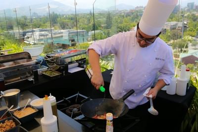 Chef cocinando junto a buffet al aire libre en la terraza rooftop de Tramonto Bar & Terrace en NOI Vitacura