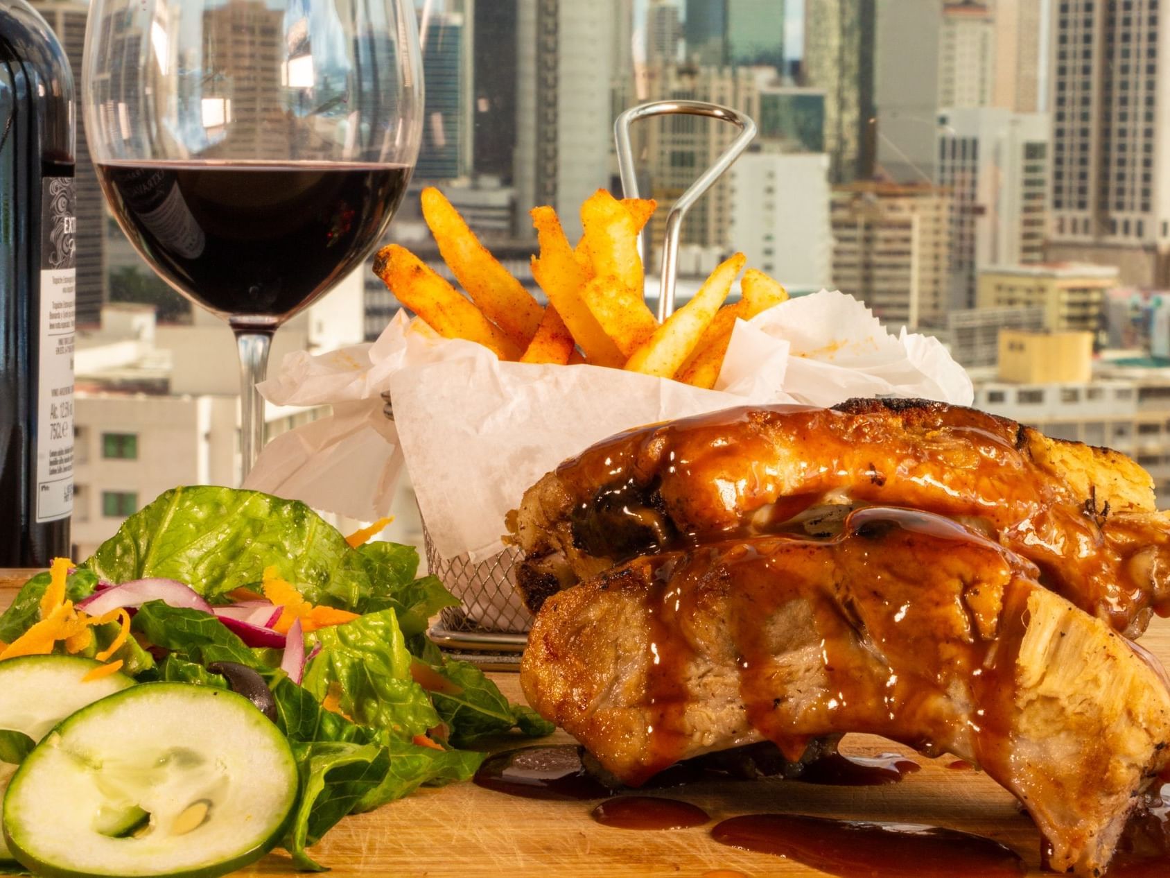 A dish of ribs served with french fries, a salad and a glass of red wine 