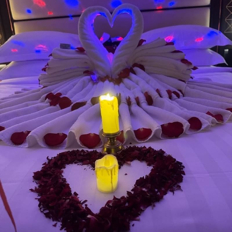 Room at Warwick Hotels and Resorts, decorated for a romantic evening with rose petals, candles, and a towel swan on the bed