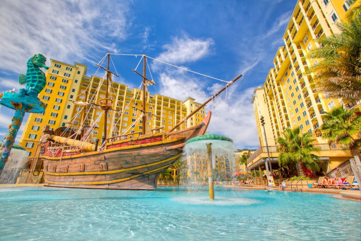 A large pool with a fountain and a ship in the middle, surrounded by buildings and balconies.