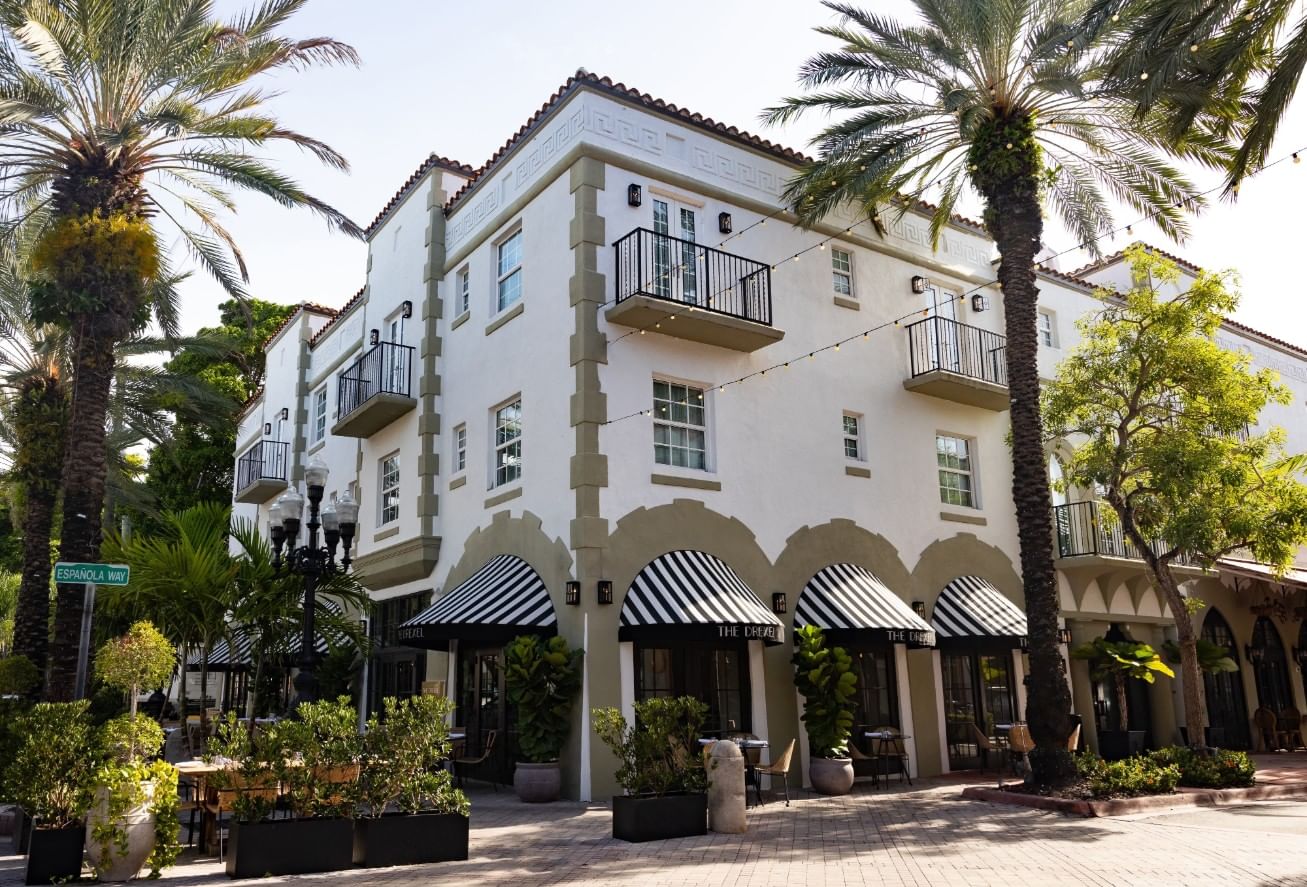 A white, multi-story building with balconies and palm trees in front.