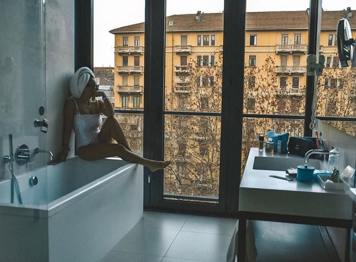 Donna con asciugamano sulla testa in una vasca da bagno di fronte ad una finestra su DUPARC Contemporary Suites