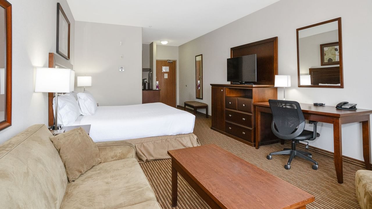 Hotel room with a king bed and a sofa bed, TV, work desk, chair, and coffee table
