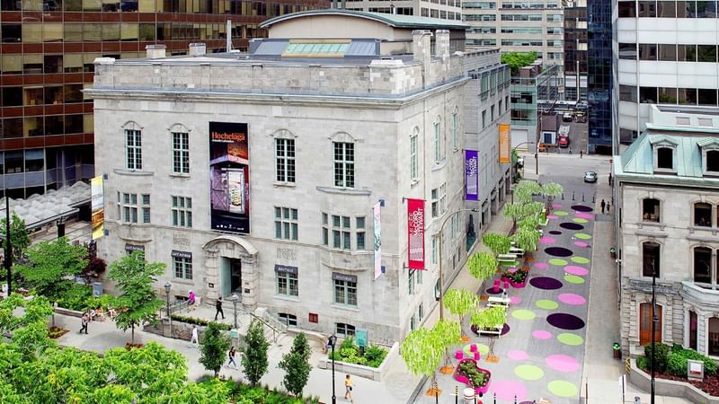 Aerial view of a historic stone museum building with colorful circular pavement art and urban plaza at Warwick Le Crystal Montreal
