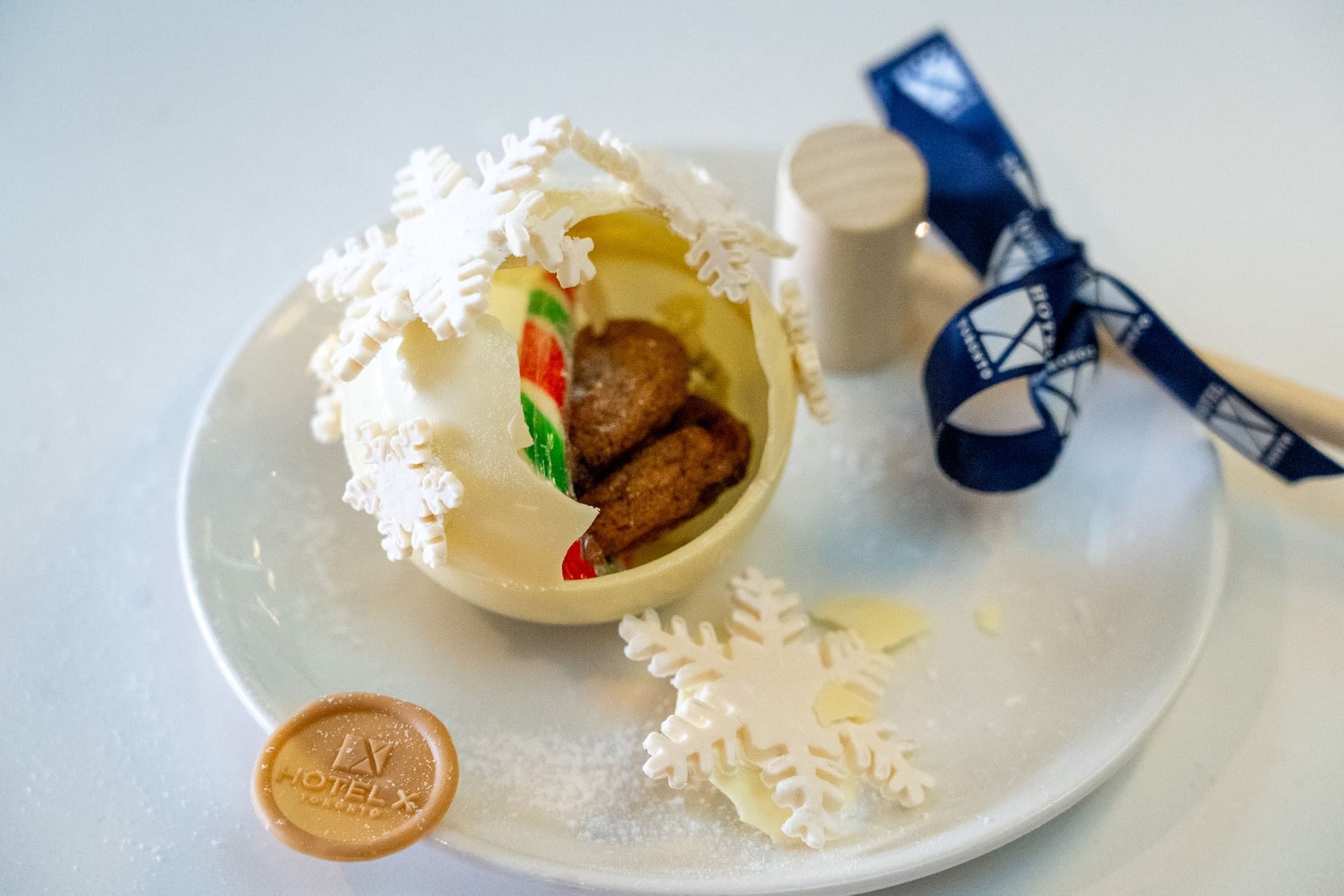 Holiday chocolate sphere with cookies and candy by white snowflake decorations arranged on a plate at Hotel X Toronto