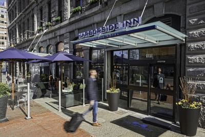 Guests dining at outdoor patio tables under purple umbrellas near the main entrance at Harborside Inn Boston